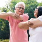 Senior,Man,Assisting,His,Wife,During,Warming,Up,Exercises,For