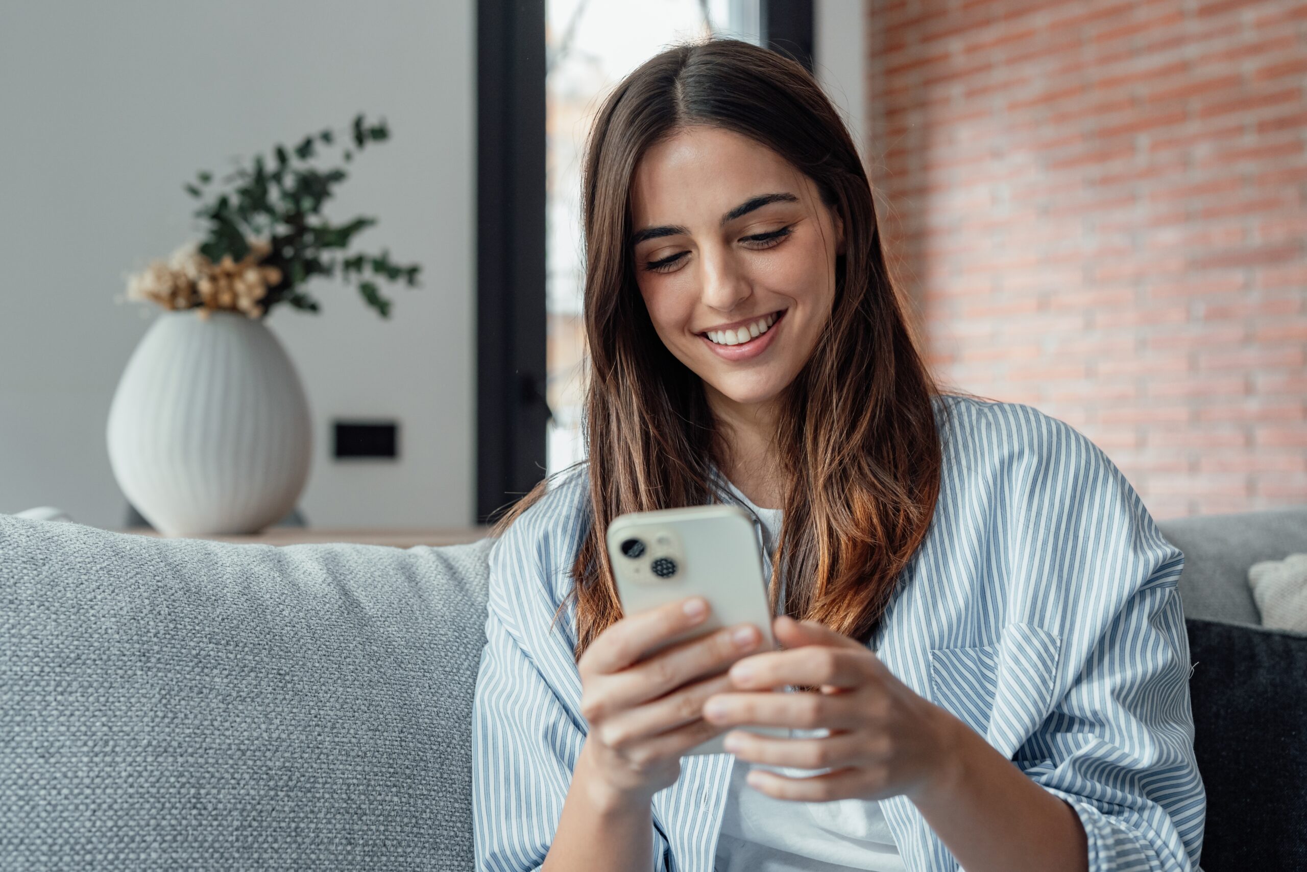 Smiling,Woman,Looking,At,Smartphone,Screen,,Sitting,On,Couch,,Enjoying
