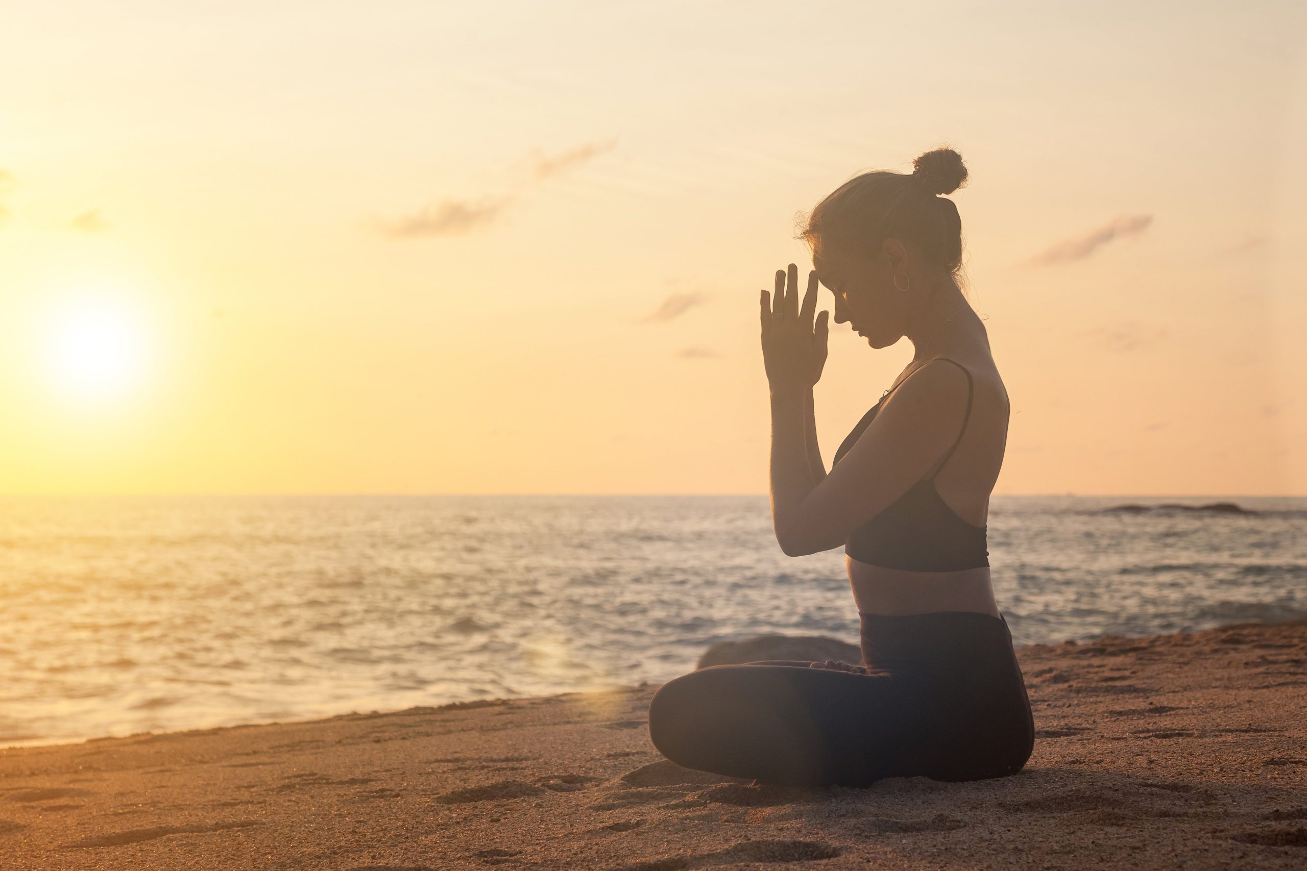 Woman meditating on beach at sunrise, mindfulness, calm breathing and wellness.