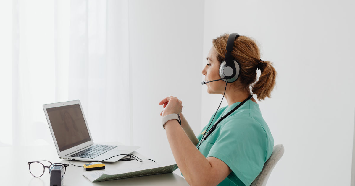 Healthcare practitioner wearing a headset during a telehealth consultation on laptop.